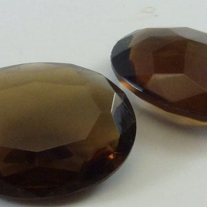 Puede incluir: Dos piedras preciosas de cuarzo ahumado de forma ovalada facetadas. Las piedras preciosas son de color marrón oscuro y tienen un acabado liso y pulido.