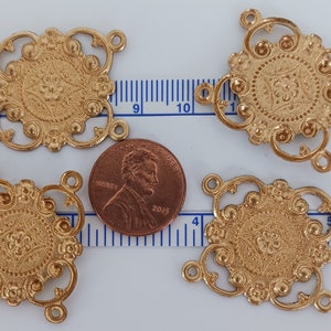 May include: Five gold-toned metal decorative embellishments with intricate designs. Each embellishment has four loops for attaching to a project. The embellishments are approximately the size of a US penny.