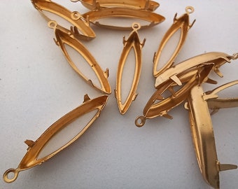 May include: A group of ten gold-colored metal oval-shaped pendant settings with a white backing. The settings are designed to hold a cabochon stone.