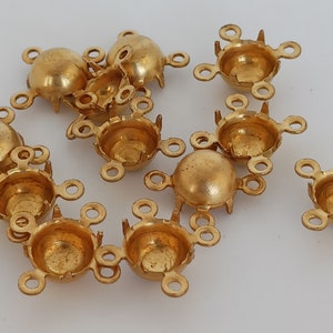 May include: A group of 10 gold-toned metal bead caps with four loops on each. The bead caps are designed to hold a round bead in the center.