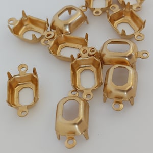 May include: A collection of gold-colored metal jewelry findings. Each finding has an octagonal opening, four prongs, and a loop for attaching to other components. These findings are likely used for setting gemstones or creating jewelry.