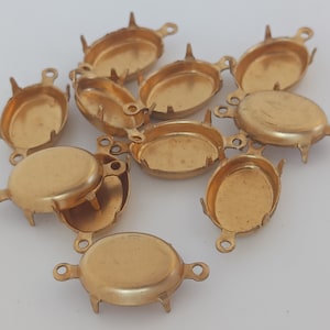 Könnte beinhalten: Eine Gruppe von zehn ovalen, goldfarbenen Metallfassungen mit Zinken und Ösen. Die Fassungen sind zum Befestigen von Cabochons oder anderen Flachsteinen geeignet.