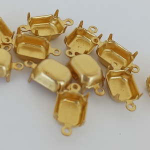 May include: A group of 10 gold-toned metal settings for square or rectangular cabochons. Each setting has a loop on the top for attaching to a chain or other jewelry piece.
