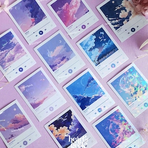 May include: A set of ten digital music player stickers featuring various pastel-coloured landscapes with clouds and moons. The stickers have a holographic finish and feature the text "heart of geek" and song titles like "Dream", "Wonder", "Twilight", "Relaxation", "Escape", "Nature", "Daydream", "Dusk", "Ethereal", and "Dawn".