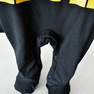 May include: Black baby onesie with yellow lettering that says "F.I.E.S.T.A." The onesie has snaps at the crotch and on the legs.