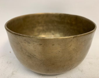 May include: A vintage brass bowl with a worn, aged patina. The bowl is round and has a smooth, slightly curved surface. It is a traditional style bowl, perfect for decorative purposes.