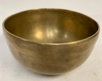 May include: A brass singing bowl with a hammered finish. The bowl is round and has a slight lip around the top.