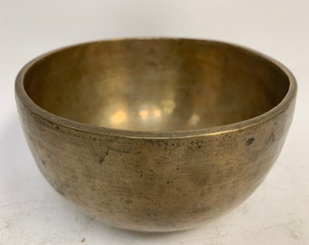 May include: A large, antique brass singing bowl with a worn, aged finish. The bowl has a wide, rounded base and a slightly flared lip.