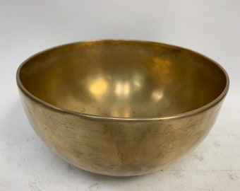 May include: A large, round, brass singing bowl with a smooth, polished surface. The bowl has a slightly worn appearance, with some scratches and marks on the surface.