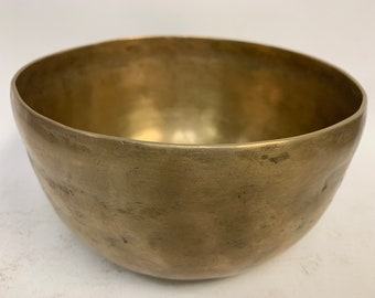 May include: A brass singing bowl with a worn, aged finish. The bowl is round and has a slightly flared lip.
