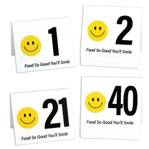 May include: Four white table cards with black numbers and a yellow smiley face. The text on the cards reads "Food So Good You'll Smile". The numbers on the cards are 1, 2, 21, and 40.
