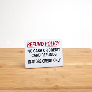 May include: White sign with red text that reads "Refund Policy" and "No cash or credit card refunds. In-store credit only."