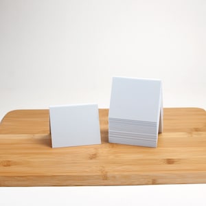 May include: A stack of white blank cards on a wooden cutting board. The cards are folded in half and stand upright.