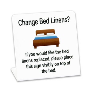 May include: White sign with the text "Change Bed Linens?" and a cartoon illustration of a bed. The text below the image reads "If you would like the bed linens replaced, please place this sign visibly on top of the bed."
