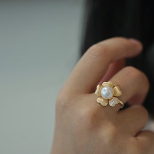 May include: A gold ring with a pearl and small diamonds in the center, shaped like a flower with five petals.