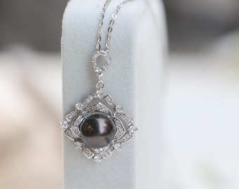 May include: A silver necklace with a black pearl pendant set in a diamond-shaped frame with smaller diamonds around the pearl.