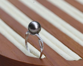 May include: A silver-toned ring featuring a single round dark gray pearl set at the top. The band is split into two delicate arms that cross beneath the pearl, with one arm accented by a row of small, clear, sparkling stones along the side.