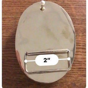 May include: Silver belt buckle with a 5.1 cm wide strap opening. The buckle is round and has a smooth, polished finish.