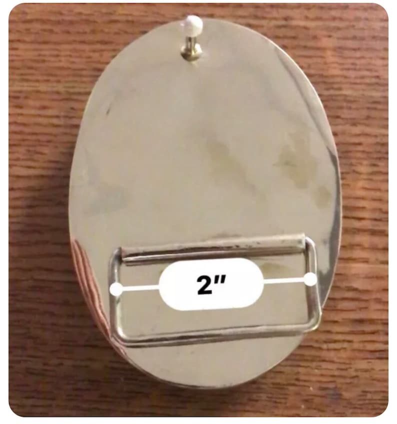 May include: Silver belt buckle with a 5.1 cm wide strap opening. The buckle is round and has a smooth, polished finish.