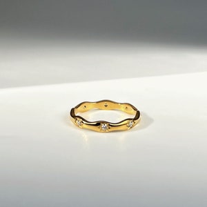 May include: A gold ring with a wavy band and small clear stones set into the band.