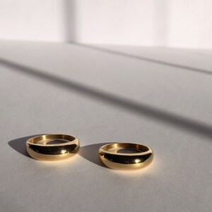 May include: Two gold-coloured rings with a rounded, slightly domed shape. The rings are on a white surface.