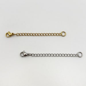 May include: Two necklace extender chains, one in a gold tone and one in a silver tone. Each extender features a series of interconnected oval links, a lobster claw clasp at one end, and a small circular jump ring at the opposite end.