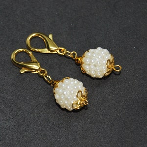 Peut inclure: Deux porte-clés dorés avec des perles blanches ressemblant à des perles regroupées en forme ronde. Chaque porte-clés a un fermoir doré.