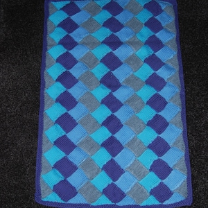 May include: A knitted blanket with a diamond pattern in shades of blue and grey. The blanket has a dark blue border.