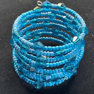 Può includere: Un braccialetto a spirale nei toni del blu. Il braccialetto è composto da piccole perline rotonde e perline di cristallo sfaccettate più grandi. Il braccialetto si avvolge più volte, creando un effetto a strati. Il braccialetto ha un diametro di circa 5 cm.