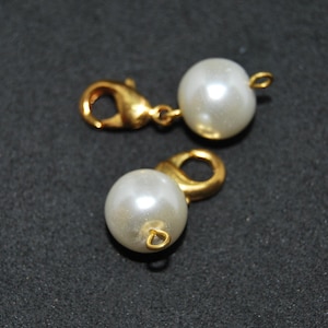 May include: Two gold-toned clasps with white pearl accents. Each clasp has a loop on one end and a hook on the other.