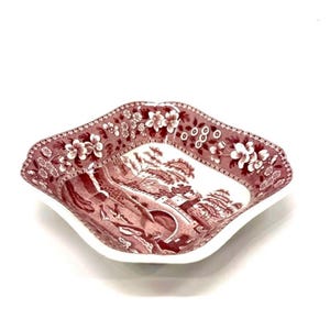 May include: A square decorative dish with a white interior and a maroon floral and landscape design around the rim and on the interior. The dish has a scalloped edge and is set against a white background.