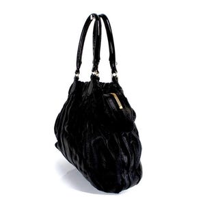 Puede incluir: Bolso de mano de cuero negro con superficie texturizada y cremallera dorada. El bolso tiene dos asas negras y forma redondeada. El bolso est&aacute; sobre un fondo blanco.