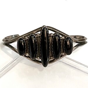 May include: A silver bracelet with a black onyx stone design. The bracelet is made of sterling silver and features a unique design with a central black onyx stone surrounded by smaller black onyx stones.