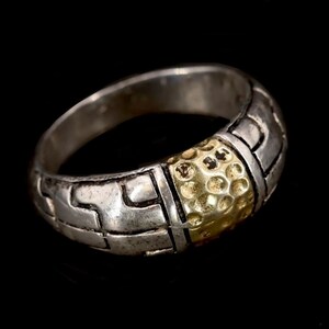 May include: A silver ring with a gold band. The ring is decorated with a geometric pattern.