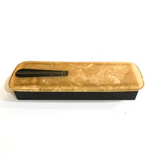 May include: A rectangular box with a marbled, cream-colored lid and a black handle. The box is made of plastic and has a black base.
