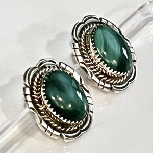 May include: A pair of silver earrings with green stone cabochons set in a detailed silver bezel. The stones have a swirling pattern and are oval shaped.