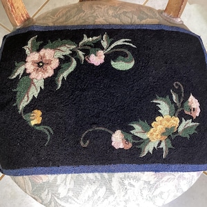 May include: A black chair cushion with a floral design embroidered on it. The flowers are pink, yellow, and green. The cushion has a blue border.