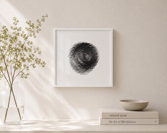 May include: A framed black and white abstract art print. The artwork features a textured, circular design in shades of black and gray. The print is displayed in a white frame, and rests on a neutral-toned surface. A small, gray bowl and two books are also on the surface.