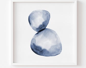 May include: A square white frame containing a watercolor painting of two stacked, rounded abstract shapes in varying shades of indigo blue. The upper shape is smaller and lighter, while the lower shape is larger and darker, set against a white background.
