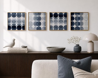 May include: Four framed abstract art prints with a repeating pattern of overlapping blue circles. The prints are in gold frames and hang on a white wall above a dark wood cabinet. A white bird statue and books are on the cabinet.