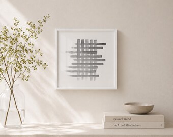 May include: A framed abstract art print featuring a gray watercolor design of intersecting horizontal and vertical lines. The artwork is in a white frame. A small, light-colored bowl and two books are on a shelf below the artwork.
