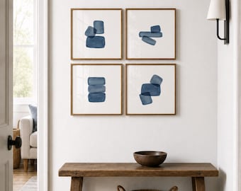 May include: Four framed abstract art prints with indigo blue shapes on a white background. The prints are displayed on a white wall above a wooden bench with a woven basket and a wooden bowl.