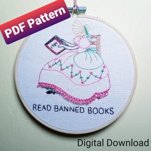 Könnte beinhalten: Stickbild in einem runden Rahmen, das eine Frau zeigt, die ein Buch mit dem Text "1984" auf dem Cover liest. Der Rahmen trägt unten den Text "READ BANNED BOOKS".