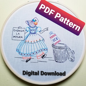 May include: Embroidered hoop art featuring a woman in a blue and white dress holding a sign that says "CHINGA LA MIGRA". She is walking away from a trash can with a bag of ice in it. The hoop is white with a black border.