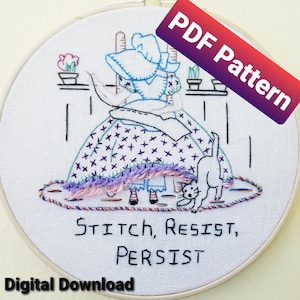 以下が含まれることがあります： 白い刺繍枠に、椅子に座った女性と猫のカラフルな刺繍が施されています。刺繍には「Stitch, Resist, Persist」という文字が書かれています。