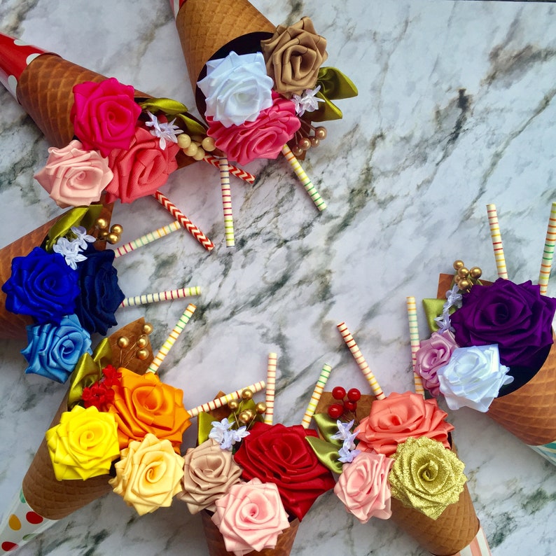 May include: A bouquet of colorful satin ribbon flowers arranged in ice cream cones. The flowers are in shades of red, orange, yellow, green, blue, purple, and white.