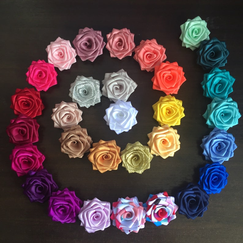 May include: A collection of 25 handmade satin fabric rose flower embellishments in various colors, including pink, red, orange, yellow, green, blue, purple, and white. The roses are arranged in a spiral pattern.