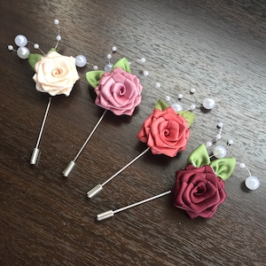 May include: Four fabric rose brooches with pearl accents. The roses are in shades of pink and burgundy. The brooches are attached to silver pins.