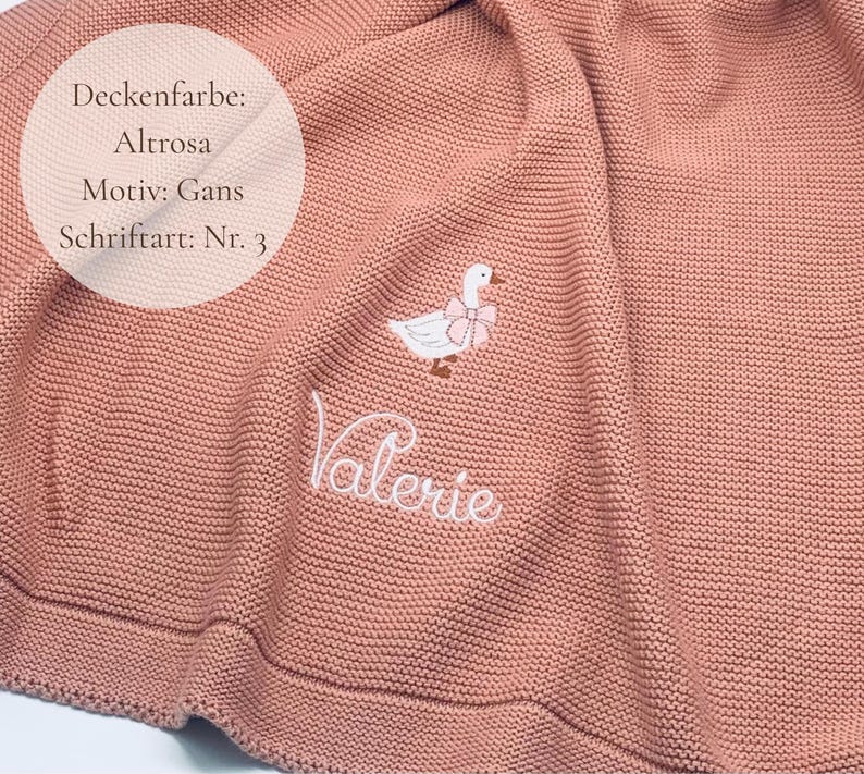 May include: A dusty pink knitted blanket featuring an embroidered white goose with a pink bow around its neck. The name Valerie is embroidered in white cursive script below the goose. Text on the image reads Deckenfarbe: Altrosa, Motiv: Gans, Schriftart: Nr. 3.