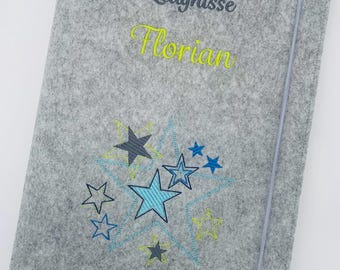 Könnte beinhalten: Eine graue Filzmappe mit der gestickten Aufschrift "Zeugnisse" in Dunkelgrau und "Florian" in Limettengrün. Unter dem Text befindet sich eine Ansammlung von gestickten Sternen in verschiedenen Blau-, Dunkelgrau- und Limettengrüntönen.
